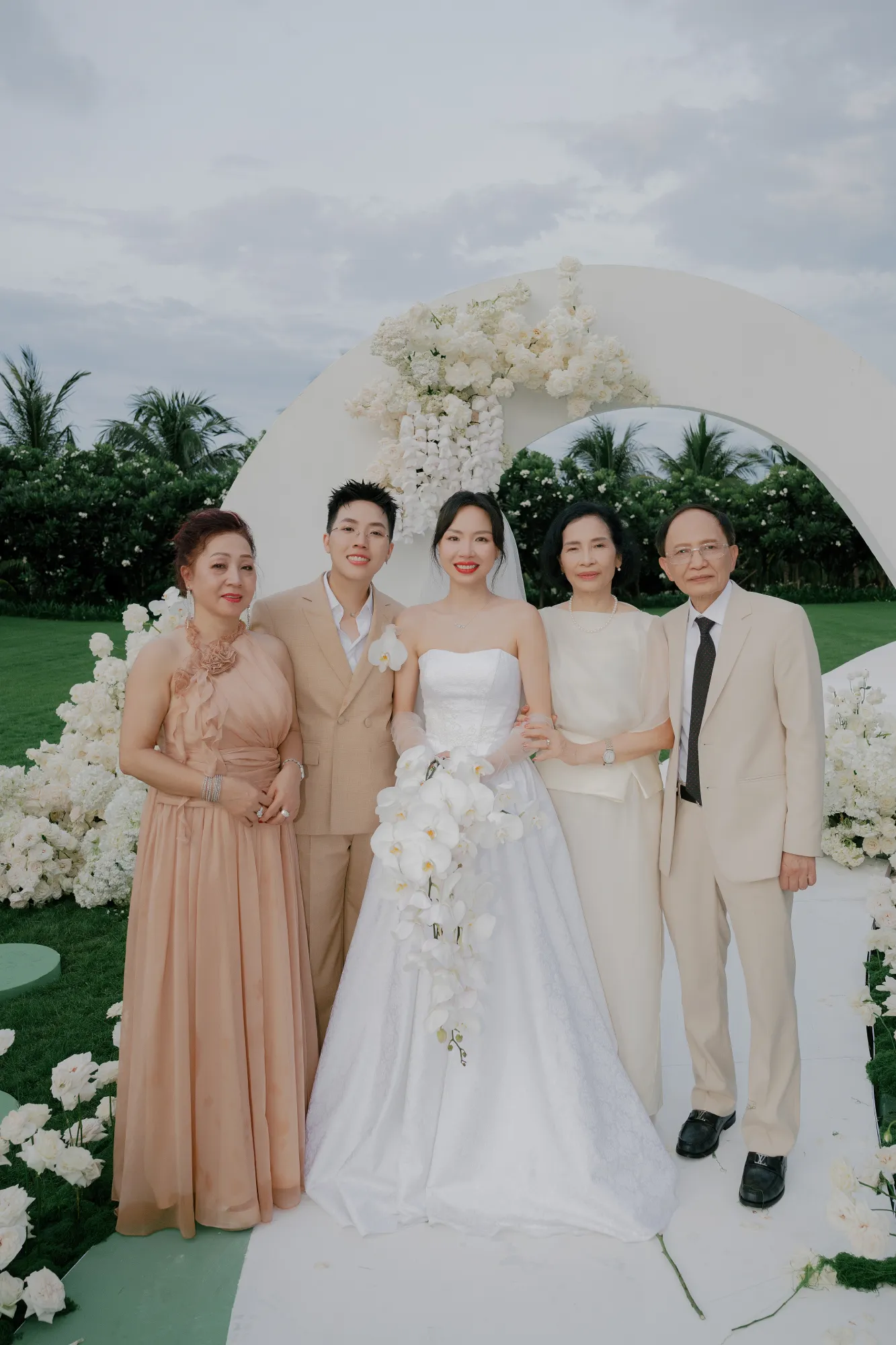 Cặp đôi chụp ảnh kỷ niệm cùng gia đình dưới cổng hoa tiệc cưới ngoài trời.