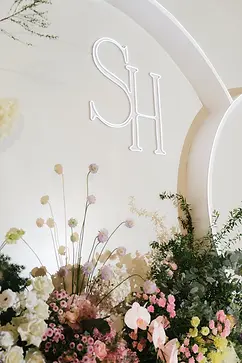 Close-up of a glowing monogram on a curved wedding backdrop surrounded by flowers.