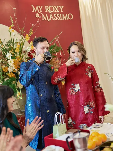 The groom sipping Vietnamese phin coffee while the bride enjoys an espresso during their unique cultural coffee exchange ritual as family members applaud
