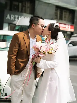 Bride and groom sharing a kiss beside a vintage car decorated with flowers.