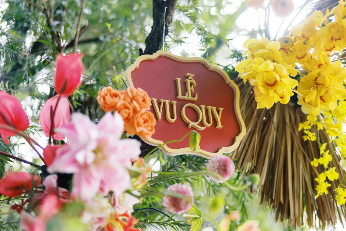 Bảng “Lễ Vu Quy” màu đỏ nổi bật giữa khung hoa tươi nhiều màu sắc, mang đậm phong cách truyền thống Việt Nam.