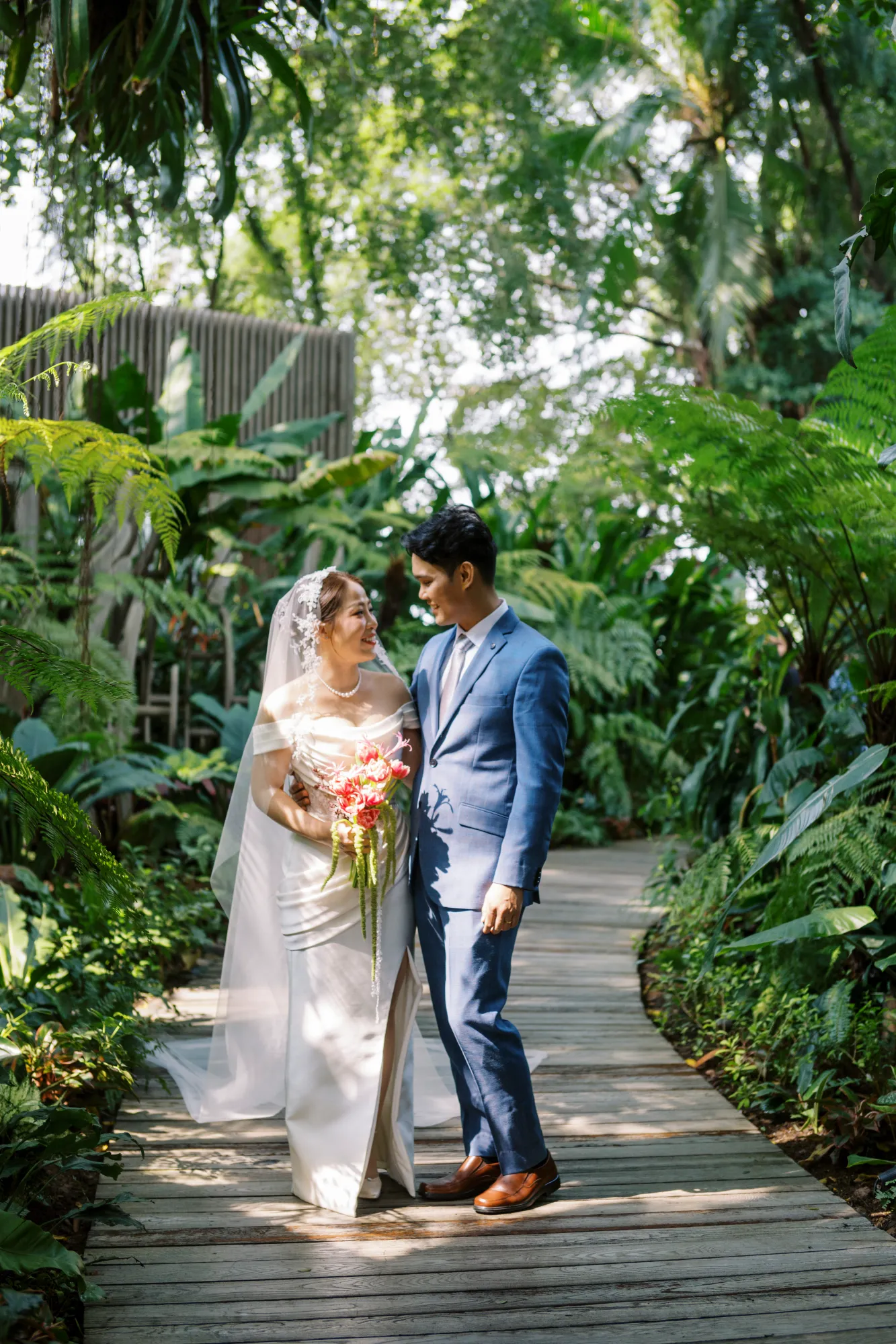 Bride and groom walking along a wooden garden path.