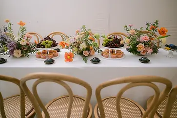 Bàn tiệc dài trang trí hoa tươi, nho và bánh nhỏ với tông màu nhẹ nhàng, phù hợp không gian tiếp khách.