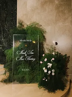 Transparent acrylic welcome sign surrounded by lush greenery and soft floral arrangements.