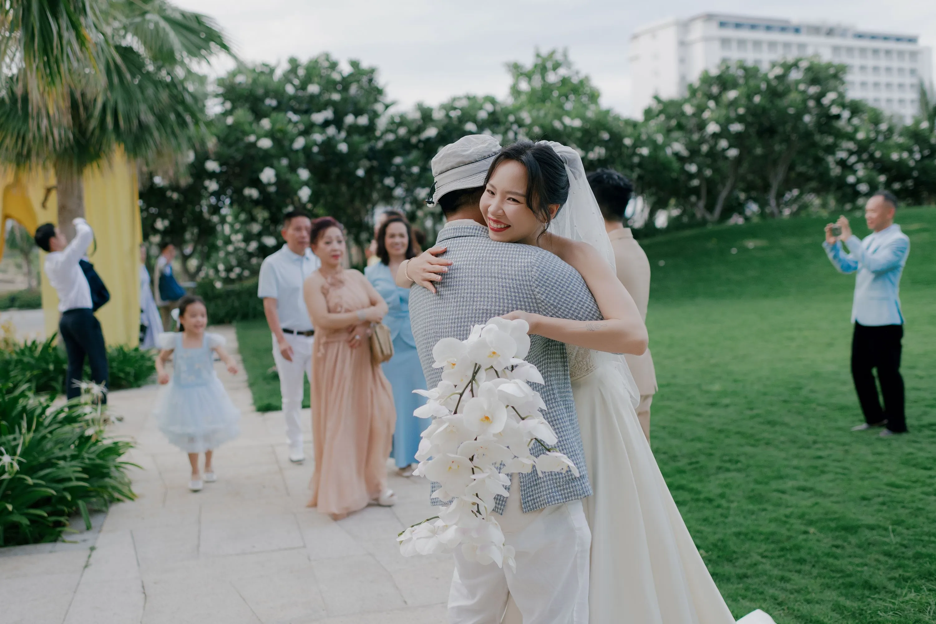 The bride warmly hugs a guest during the outdoor wedding, surrounded by greenery and smiling family members.