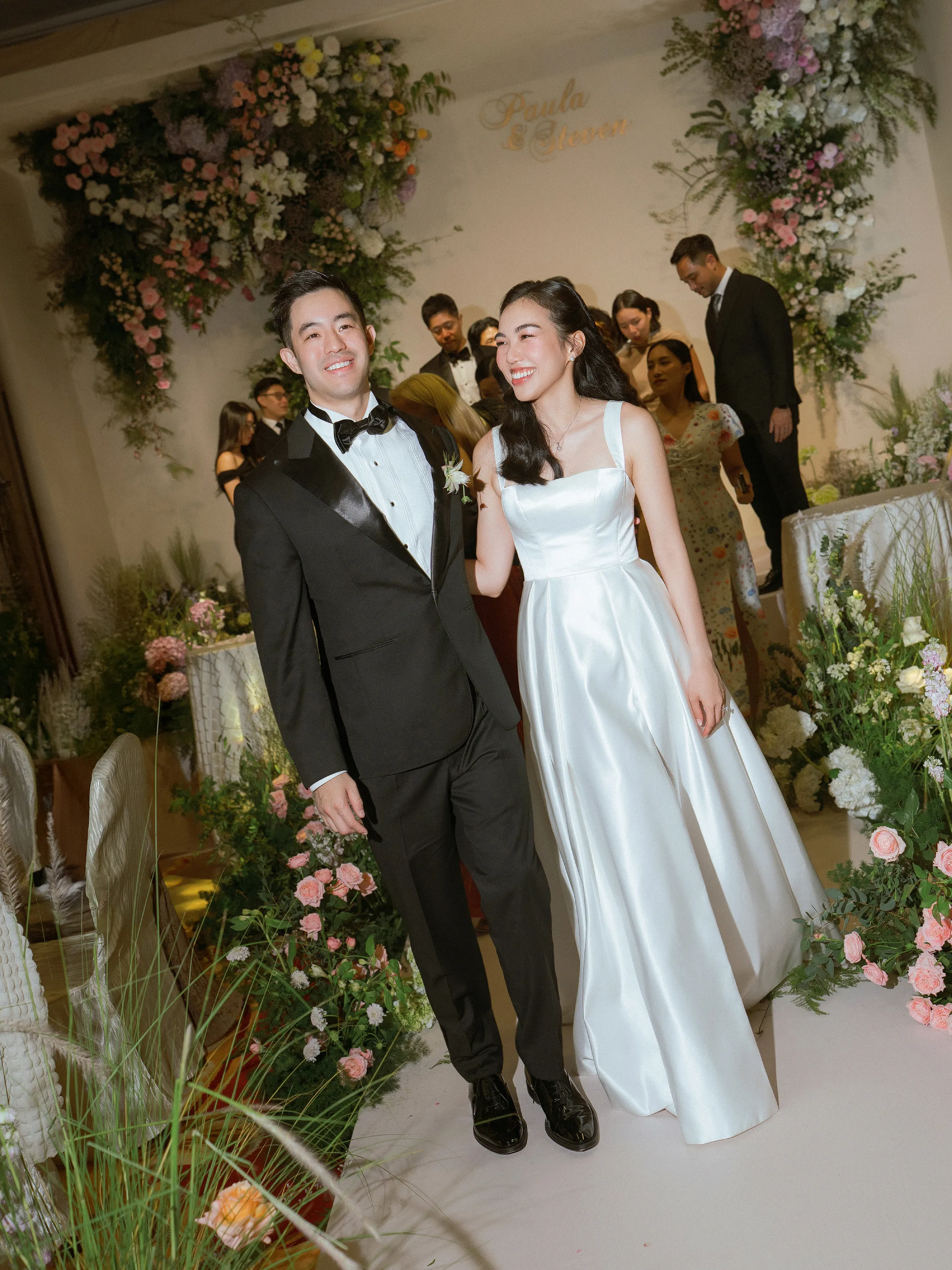 Paula & Steven tay trong tay bước trên lối hoa trong không gian lễ cưới ngập tràn ánh sáng và hương sắc của hoa tươi.