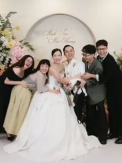 Bride and groom posing happily with close friends in front of a floral wedding backdrop.