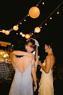 A heartfelt hug shared between the bride and her friends during a relaxed garden reception at night.