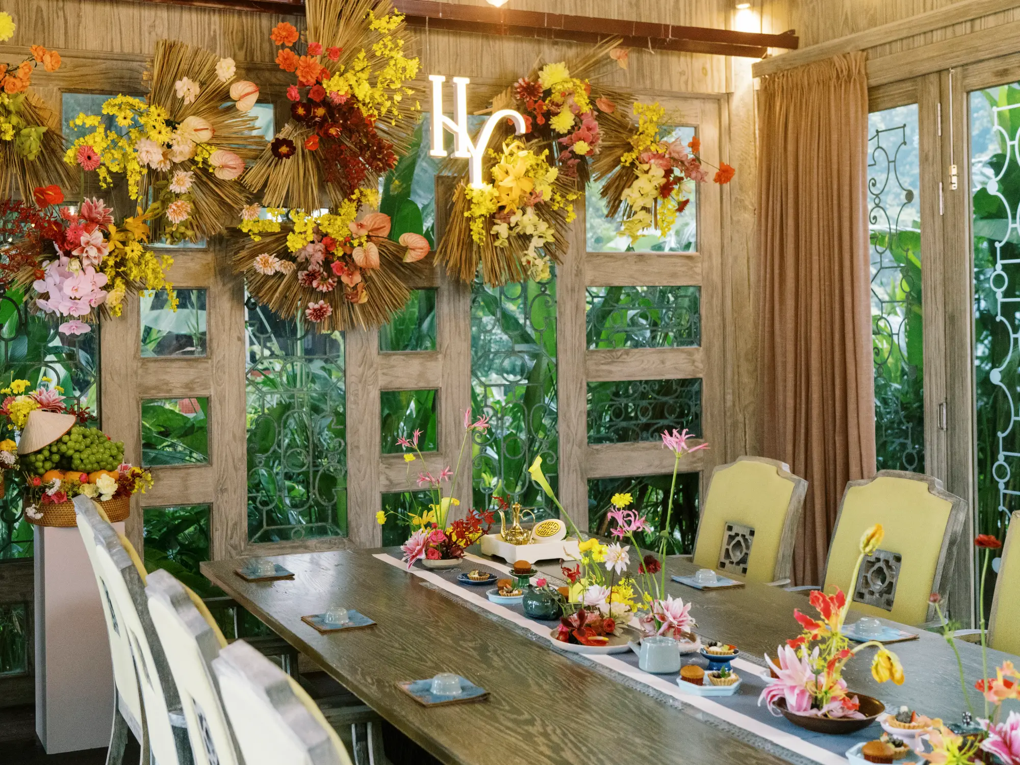 Không gian trang trí tiệc cưới sang trọng với tông màu vàng và nâu ấm, điểm xuyết hoa tươi rực rỡ mang phong cách Á Đông, tạo cảm giác gần gũi và tinh tế.