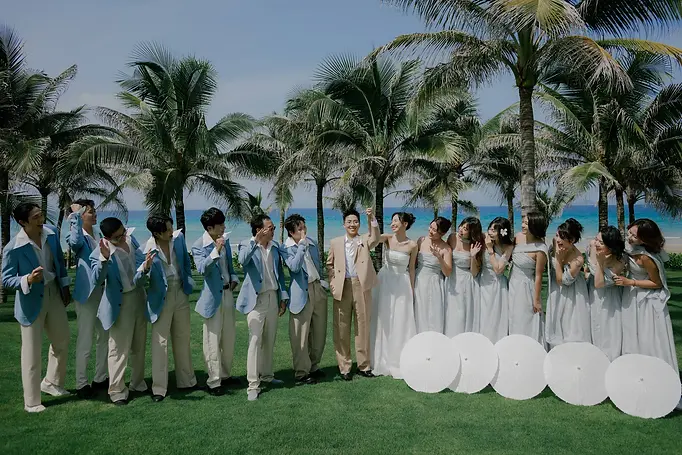 A joyful wedding party celebrating together on a tropical lawn, surrounded by palm trees and bright blue skies.
