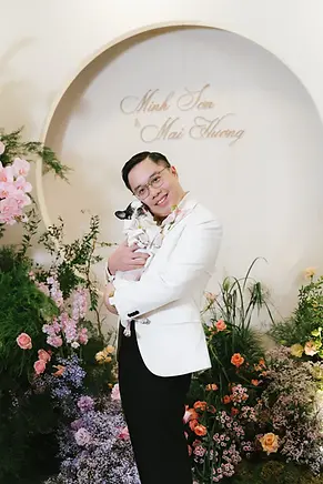 Groom smiling while holding a small dog in front of a floral wedding backdrop.