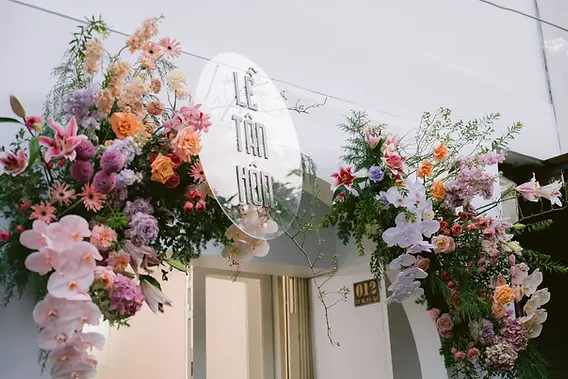 A floral entrance arrangement with a transparent sign welcoming guests to the wedding celebration.