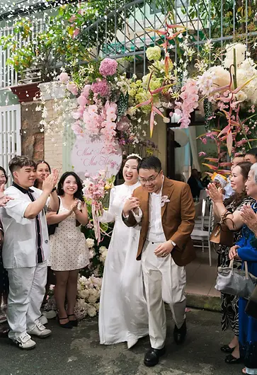 Bride and groom walking out together beneath a floral arch as guests clap and celebrate.