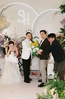 Friends presenting creative gift to couple on stage with custom floral backdrop