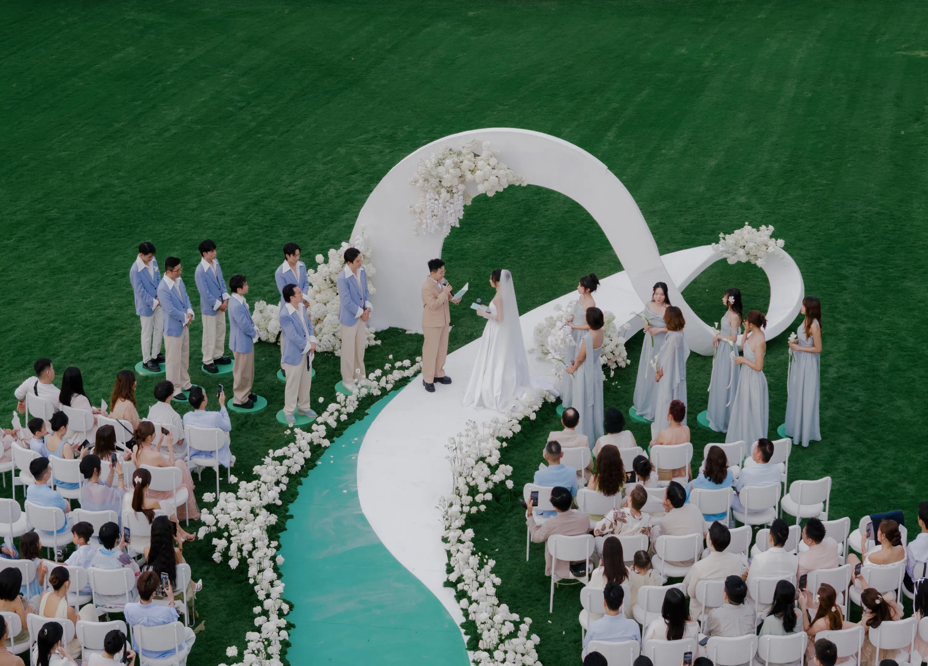 Lễ cưới ngoài trời của Kai & Hạnh với đường cong biểu tượng vô cực và lối đi phủ đầy hoa trắng, thể hiện tình yêu vĩnh cửu.