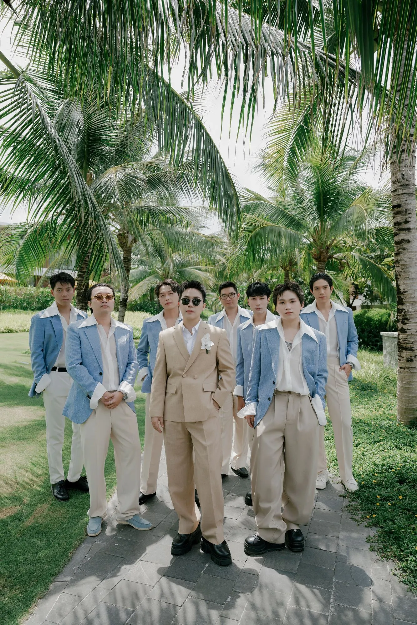 A stylish portrait of the groom and groomsmen standing beneath tall palm trees in a tropical garden.