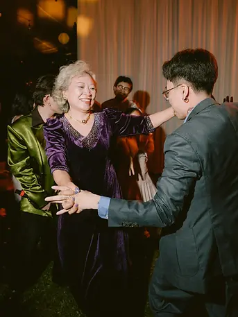 Khách mời ca hát và chung vui quanh bàn tiệc tối, ánh nến và hoa bàn tạo cảm giác ấm cúng, thân mật.