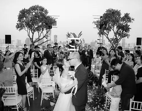 Khoảnh khắc cô dâu chú rể trao nụ hôn trong lễ cưới rooftop, xung quanh là gia đình và bạn bè vỗ tay chúc mừng