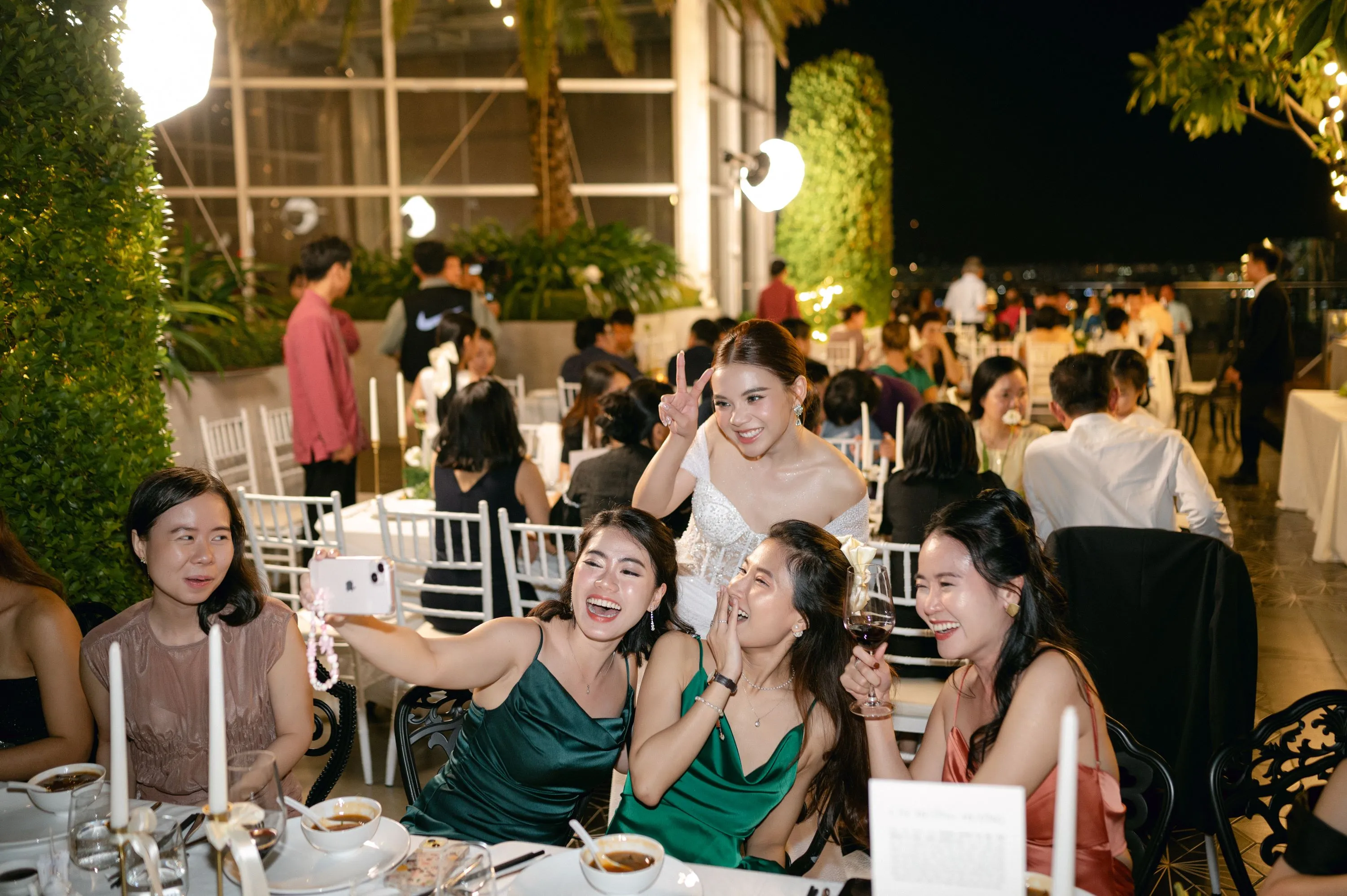 Nhóm bạn vui vẻ selfie cùng cô dâu trong bữa tiệc tối tại sân thượng lung linh ánh đèn.