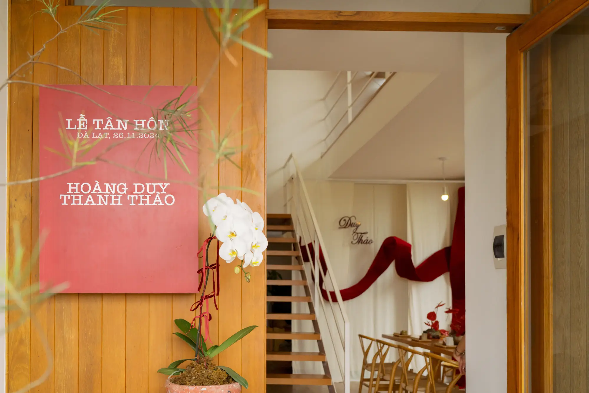Trang trí cổng nhà lễ tân hôn với bảng tên màu đỏ và hoa lan trắng, tạo ấn tượng sang trọng và ấm cúng cho ngày trọng đại.