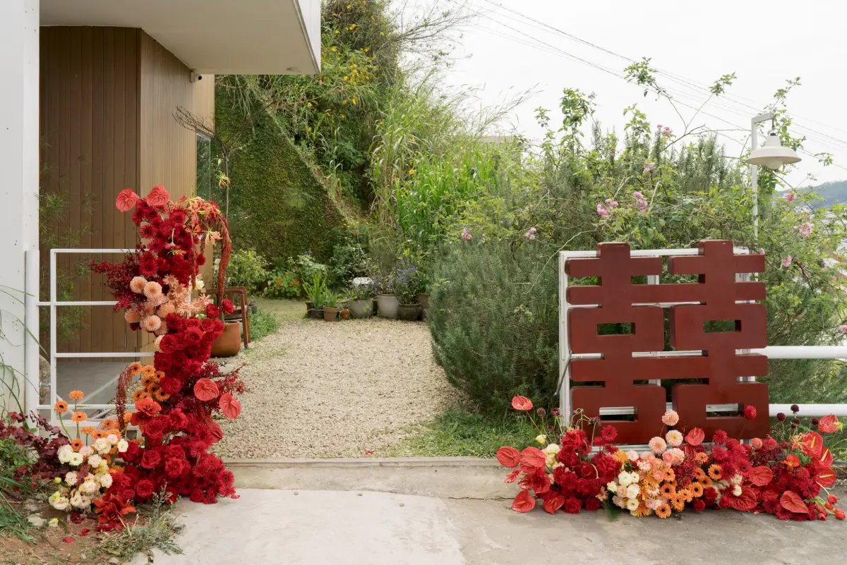 Trang trí cổng hoa cưới với tông màu đỏ rực rỡ, điểm xuyết hoa hồng và hoa cúc cam, mang đậm nét truyền thống và ấm áp trong lễ cưới Việt Nam.