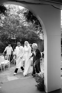 Bride and groom walking together with the groom’s mother during a wedding gathering.