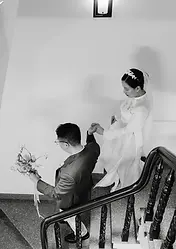 Black and white photo of a bride guiding the groom down a staircase while holding his hand.