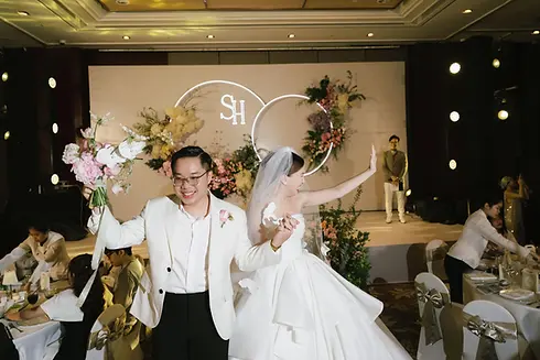 Bride and groom making their grand entrance at the reception, holding hands and waving to guests.