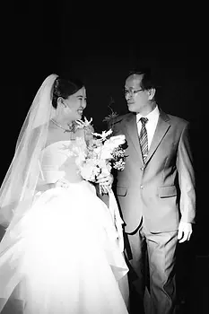 Bride walking beside her father while holding a bouquet as they enter the wedding ballroom.