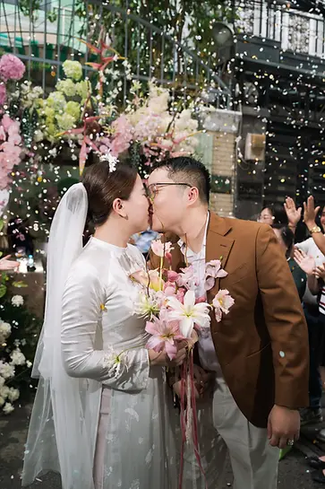 Bride and groom sharing a kiss while confetti falls around them during an outdoor celebration.