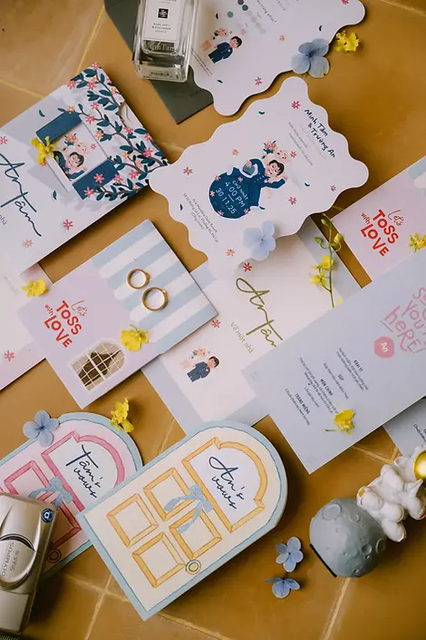 A colorful flatlay of wedding invitations, illustrated stationery, and small decorative details arranged on a table.