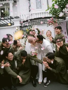 A joyful moment in the Vietnamese traditional ceremony styled by The Story Packer wedding planner, as the couple shares a kiss surrounded by friends, with flower petals falling in an outdoor celebration.