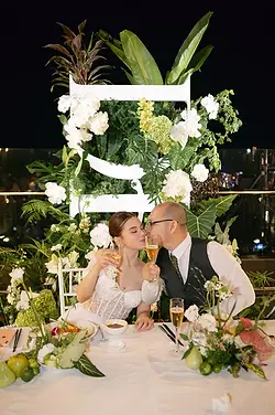 A tender moment as the couple share a kiss while holding glasses during the wedding dinner.