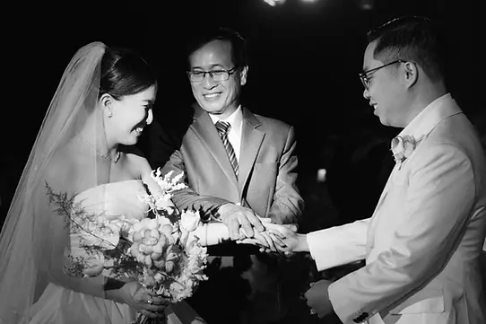 Bride and groom holding hands as the bride’s father places his hands over theirs during the wedding in Saigon.