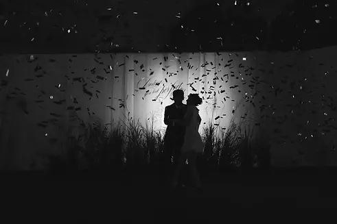 Black and white silhouette of the couple standing beneath falling confetti during their nighttime celebration.