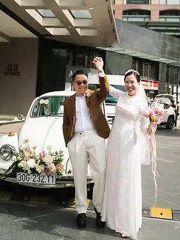 Bride and groom celebrating beside a vintage car decorated with flowers.