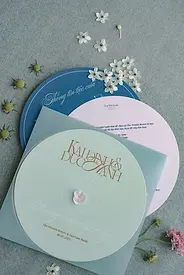Pastel round wedding invitation cards layered in blue and sage tones, styled with small white flowers on textured fabric.