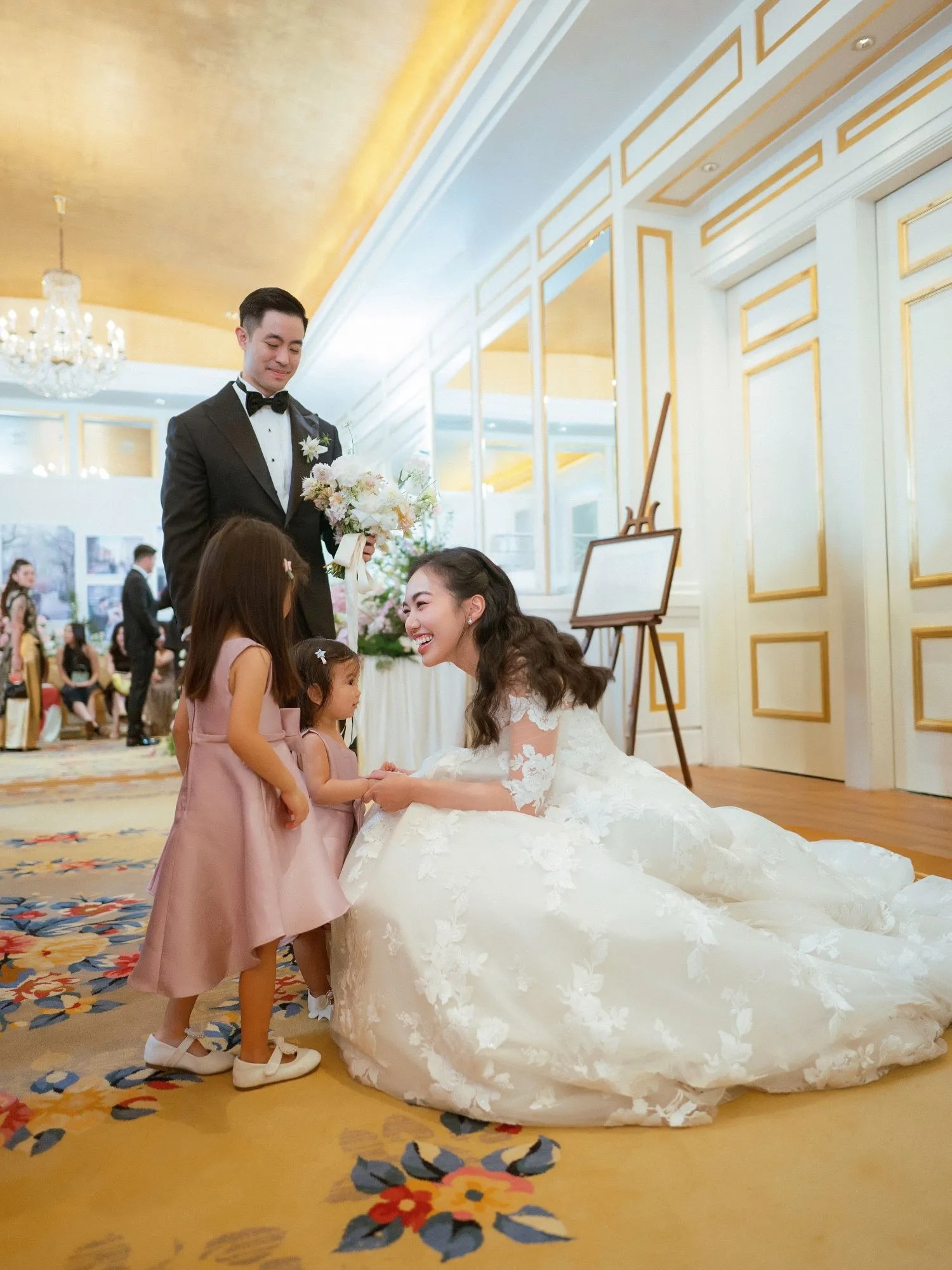 The bride smiles warmly while greeting two young girls in a beautifully decorated ballroom setting.