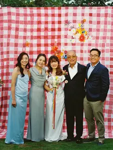 Family and couple posing at a checked red wedding photo backdrop decorated with floral accents, capturing joyful moments at an intimate celebration.