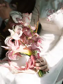 Close-up of a bridal bouquet with pink orchids and soft ribbon in warm sunlight.