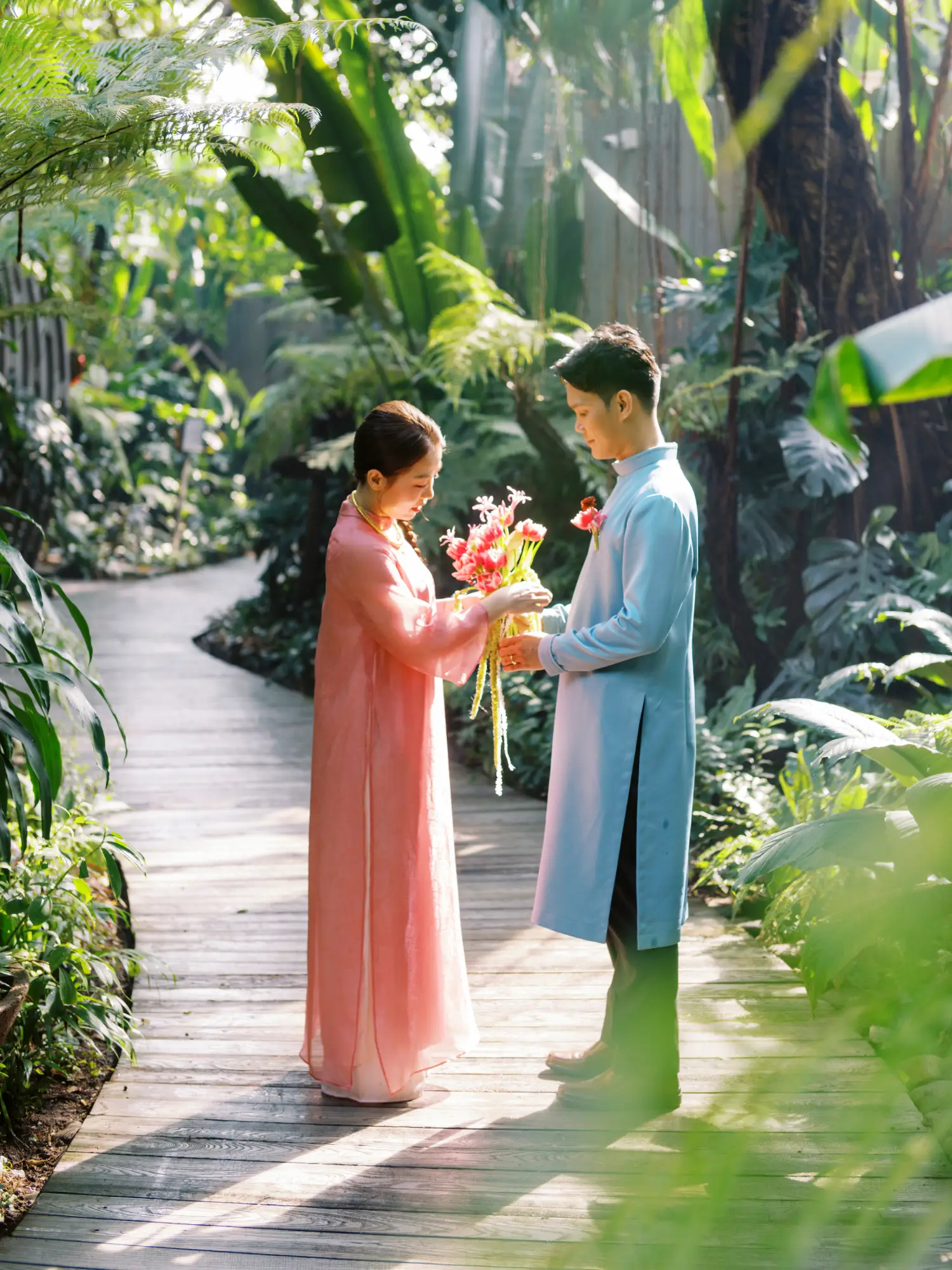 Thai - Viet couple in traditional áo dài exchanging bouquets in a garden setting before the tea ceremony.