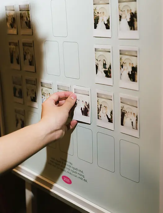Hand placing an instant photo onto a guest photo board filled with small wedding snapshots.
