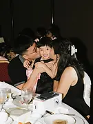 Kiss Cam 02: Parents kissing their young daughter on both cheeks while sitting at a wedding dinner table.