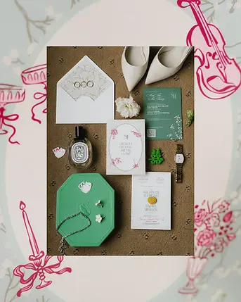 Flat lay of wedding details including invitation cards, rings, perfume, and bridal shoes.