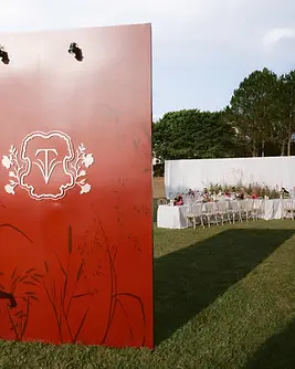 Red wedding backdrop with botanical illustrations overlooking an outdoor reception setup on the lawn.