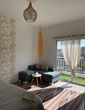 Nordisches Zimmer in Casa Jio mit hellem Ecksofa, Balkonzugang und natürlichem Licht.