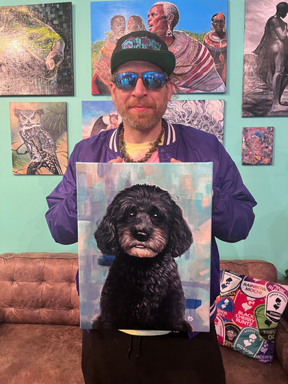 Man holding a handpainted memorial portrait of his black poodle named Charlie, surrounded by colorful artwork in a gallery setting.
