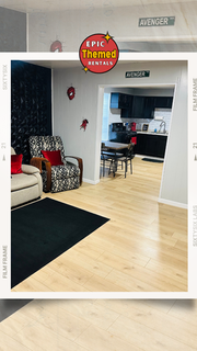 Framed photo of a Marvel-themed living room and kitchen in a vacation rental home in Amarillo, Texas, with superhero wall accents and cozy furniture by Epic Themed Rentals.