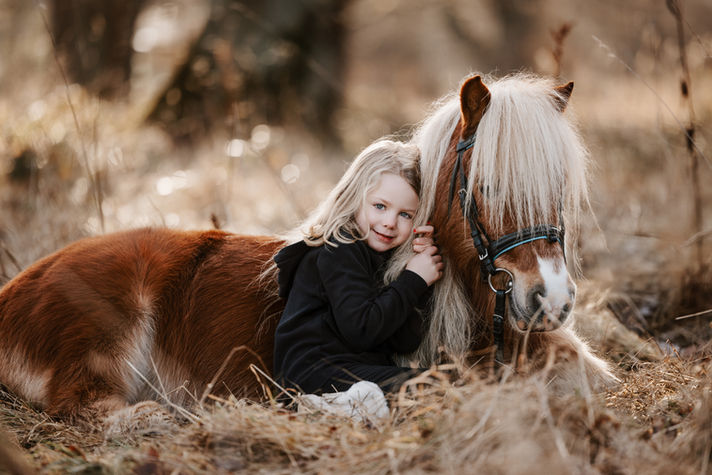 Kleines Mädchen kuschelt mit braun-weißem Pony im Herbstlicht – emotionale Kinder- und Pferdefotografie in Kassel