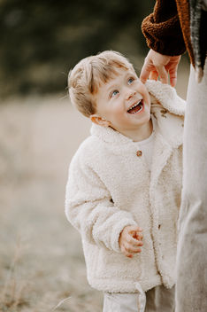 Lachender Junge in heller Jacke blickt liebevoll zu seiner Mutter auf – natürliche Familienfotografie in Kassel mit echten Emotionen von Nadine Priester.
